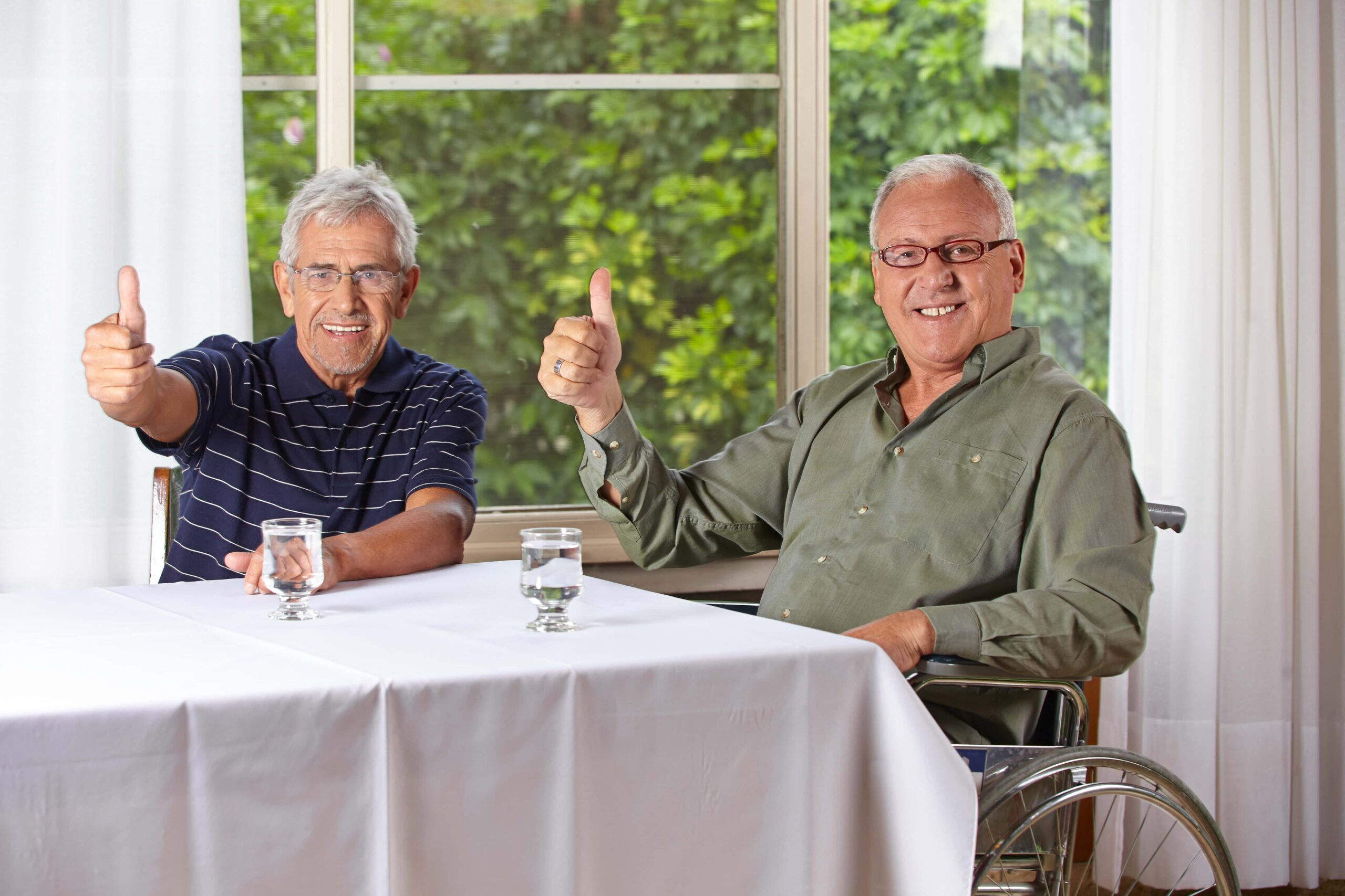 Two elder gentleman at a table with their thumbs up.