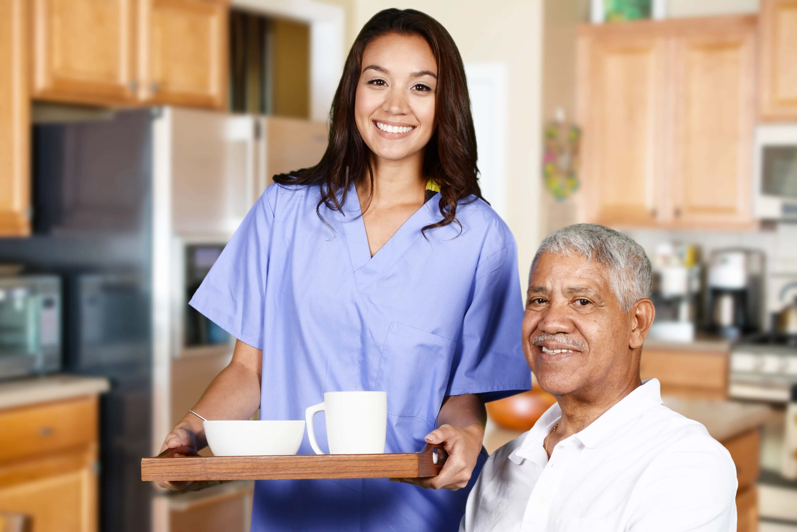 Two people, a seated elderly man and a standing younger woman with a food tray side by side with one another.
