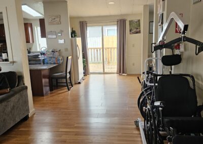 A living space with wooden floors, a kitchen on the left, sliding glass doors at the back, and two wheelchairs positioned on the right side.