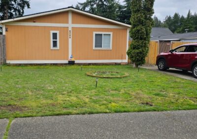 Single-story orange house with two windows, a small front yard with sparse grass, a circular garden bed, and a red SUV parked on the right side of the driveway.